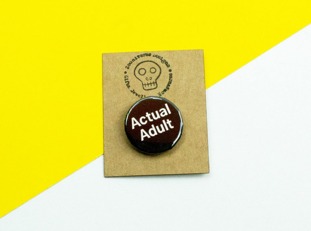 Button badge accessory with a design that says actual adult